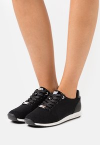 Baskets noires texturées avec bout rond, design à lacets et semelle blanche. Dotées d'accents argentés et d'un talon rembourré pour le confort.