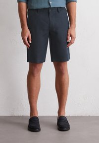 Dark blue linen shorts with a straight cut, featuring a button closure and side pockets, paired with black loafers. Smooth texture.