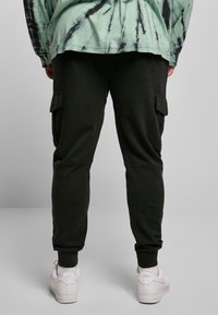 Zwarte katoenen cargo joggers met zijzakken, taps toelopende boorden en een gladde textuur, gecombineerd met witte sneakers.