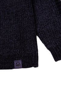 Dunkelmarineblauer, gestrickter Pullover mit geripptem Ärmel und unterem Saum sowie einem kleinen Stoffetikett, das ein schwarzes Logo auf lila Hintergrund zeigt.