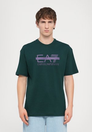 Grønn bomulls T-skjorte med et lilla trykket logo "EA7 Emporio Armani" over brystet. Korte ermer og rund halsdesign.