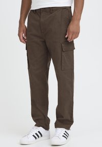 Brown cargo pants with a loose fit, featuring side pockets and a smooth, textured fabric. Paired with white sneakers and black stripes.