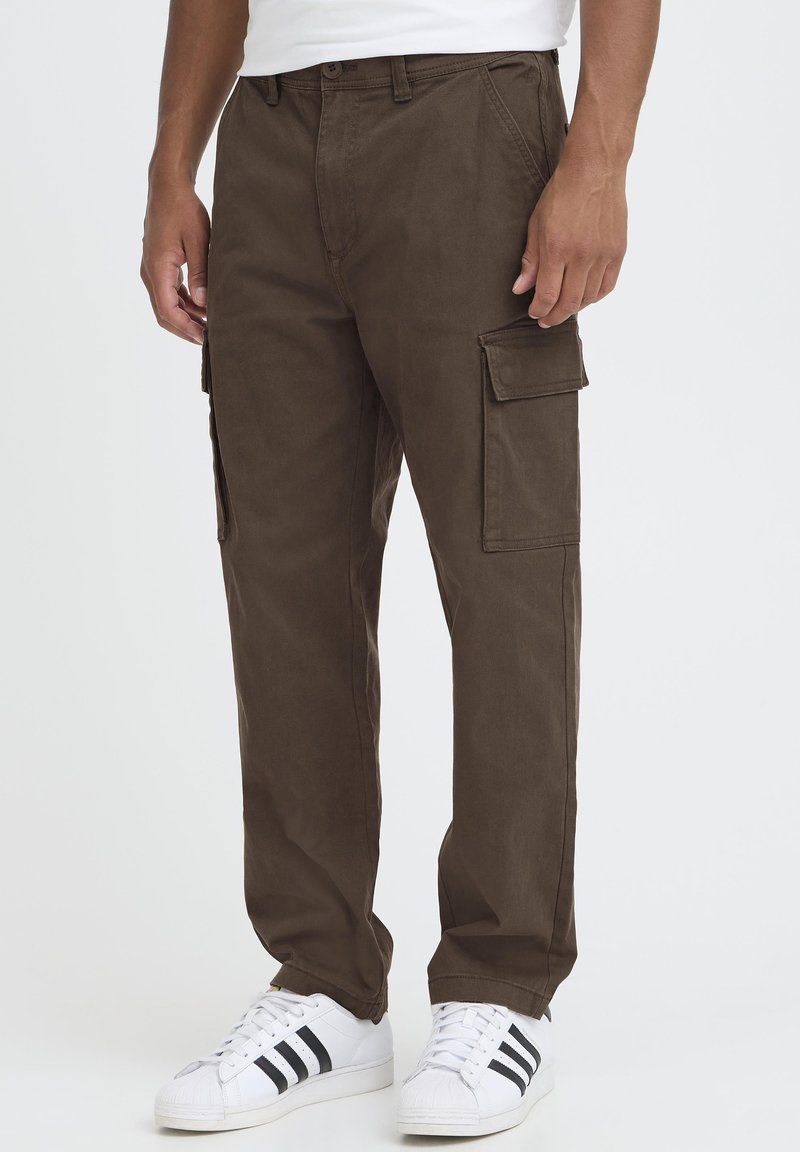 Brown cargo pants with a loose fit, featuring side pockets and a smooth, textured fabric. Paired with white sneakers and black stripes.