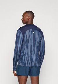 Camisola atlética de manga longa com um padrão abstrato em azul e marinho, com um painel sólido em marinho no ombro e tecido texturizado.