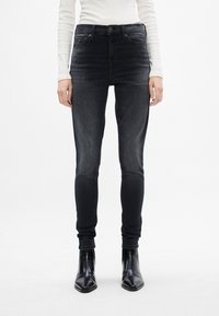 Fekete skinny farmernadrág kifakult mosással, magas derékkal, öt zsebbel és gombos záródással. Fekete, hegyes orrú bokacsizmával viselve.