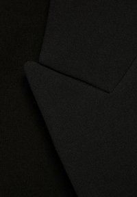 Nahaufnahme eines schwarzen strukturierten Stoffes, der sich zu überlappenden, spitzen Formen zusammenfügt und das Gewebe und die Struktur des Materials hervorhebt.