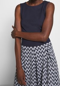 Granatowy top na ramiączkach w połączeniu z wzorzystą spódnicą z zygzakowym wzorem w granacie i bieli. Spódnica ma płynącą teksturę.
