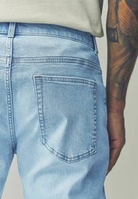 Jeans in denim azzurro chiaro con un design aderente, caratterizzati da una tasca posteriore quadrata, cuciture sottili e una texture liscia.