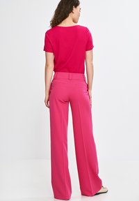 Fuksjowa bluzka z krótkim rękawem zestawiona z wysokimi spodniami o szerokich nogawkach w pasującym fuksjowym tkaninie; gładka faktura z minimalnymi detalami.