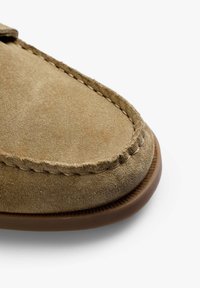 Mocassino beige in suede con punta rotonda, caratterizzato da cuciture a contrasto lungo il bordo e una suola in gomma testurizzata.