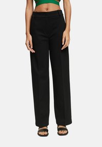 Czarne spodnie o szerokich nogawkach, wykonane z gładkiego materiału, z wysokim stanem, zapięciem na guzik oraz paskami do paska. Połączone z zielonym, krótkim topem i czarnymi sandałami.