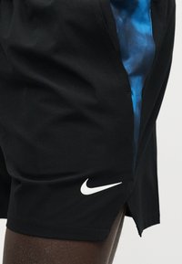 Μαύρο αθλητικό σορτς με λευκό λογότυπο Nike, που φοριέται σε σκούρο δέρμα, με μπλε υφασμάτινη ζώνη μέσης που φαίνεται από κάτω.