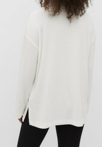 Maglione bianco a coste con maniche lunghe, caratterizzato da spacchi laterali all'orlo. La texture è morbida e lavorata a maglia, offrendo una vestibilità rilassata.