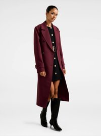 Burgundi pikema jakk topeltkinnise disaini, suurte krae ja nööpide detailidega, kantud musta kleidi ja põlvikuni mustade saapadega.