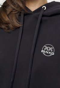 Svart hoodie i mjukt tyg. Har en dragsko på huvan, silverfärgad logotyp på bröstet och en enkel design med avslappnad passform.