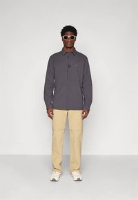 Pilka marškinėliai su kišene priekyje, derinami su smėlio spalvos krovinių kelnėmis. Yra subtili mėlyna detalė ir įprastas kirpimas. Dėvimi balti sportbačiai.