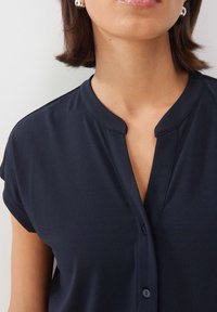 Navy blue blouse with a collar, short sleeves, and a buttoned front. Soft, smooth texture with a subtle sheen.