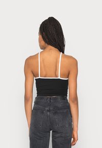 Top cropped preto com alças brancas, design ajustado, usado com jeans escuros de cintura alta com bolsos traseiros e um acabamento texturizado.