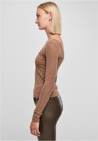 Braunes, geripptes Langarmoberteil mit taillierter Silhouette, breitem Ausschnitt und strukturiertem Stoff, kombiniert mit dunkelbraunen, enganliegenden Hosen.