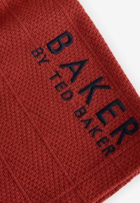 Červená texturovaná tkanina s tkaným vzorem s embosovaným tmavě modrým nápisem "BAKER by TED BAKER."