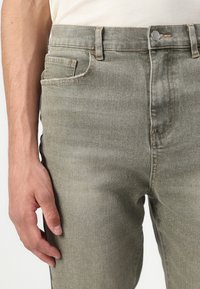 Jeans din denim verde măsliniu, cu talie standard, buzunare frontale și detalii discrete de cusătură. Materialul are un finisaj moale, ușor texturat.