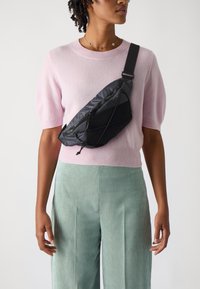 Schwarze Nylon-Schultertasche mit einem eleganten Design, das eine strukturierte Oberfläche, ein Reißverschlussfach und einen verstellbaren Gurt umfasst, der über den Körper getragen wird.