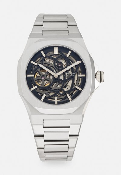 Montre en acier inoxydable argenté avec un cadran squeletté, mettant en valeur des engrenages complexes sur un fond noir. Dotée d'un boîtier géométrique et d'un bracelet à maillons.