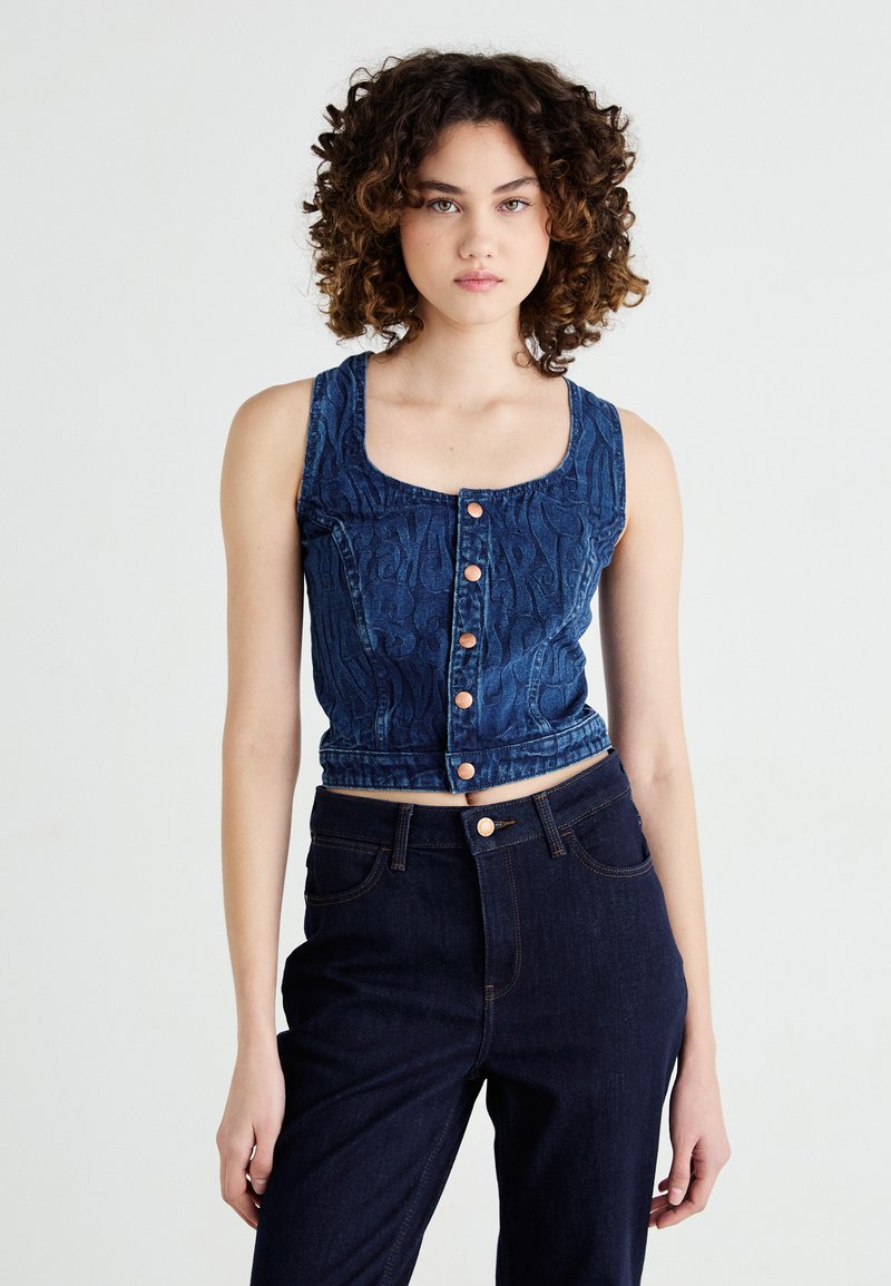 Top corto in denim con un motivo testurizzato, scollatura quadrata e cinque bottoni di rame. Abbinato a pantaloni in denim scuri a vita alta.