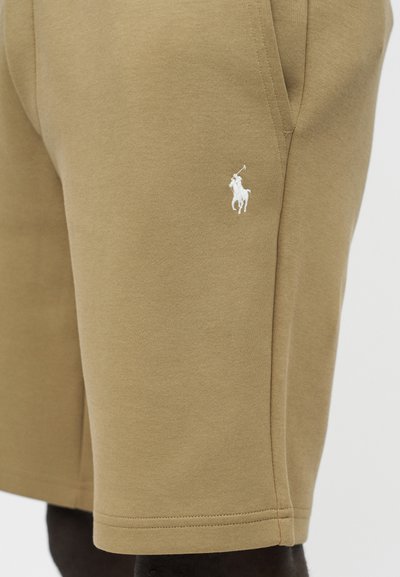 Κοντινό πλάνο σε μπεζ σορτς με πλαϊνή τσέπη και λευκό κεντημένο λογότυπο παίκτη πόλο στον μηρό.