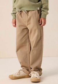 Beige wijde pantalons met een trekkoord in de taille en zakken, gecombineerd met lichtgekleurde sneakers met textuur op de zolen en veters.