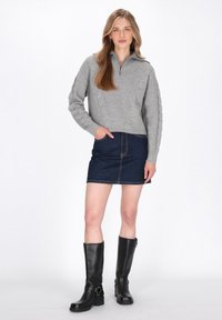 Pulover gri tricotat cu guler cu fermoar până la jumătate, asortat cu o fustă din denim și cizme negre din piele, până la genunchi, cu catarame.