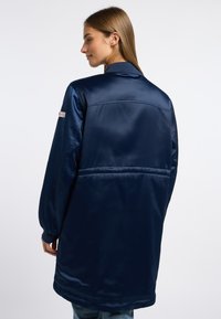 Marine satijnen jasje met een relaxte pasvorm, geribde manchetten en achterdetails. Heeft een minimalistisch ontwerp en een gladde, glanzende textuur.