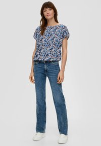 Bloemenprint top met korte mouwen, in blauw en roze tinten, relaxed fit; gecombineerd met hoog-gewelfde lichtblauwe jeans en witte sneakers.