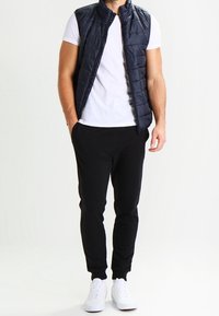 Laivastonsininen untuvatakki valkoisen T-paidan päällä, yhdistetty mustiin jogger-housuihin ja valkoisiin tennareihin. Varustettu vetoketjulla ja resoreilla hihoissa.