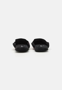 Pantofole nere in peluche con una texture morbida, aperte sul retro e con punta tonda. L'interno presenta etichette logo sulla soletta. Design semplice.