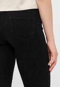 Svart denimjeans med bakficka, slim fit och en slät textur. Midjebandet sitter ovanför höfterna och har inga synliga dekorationer.