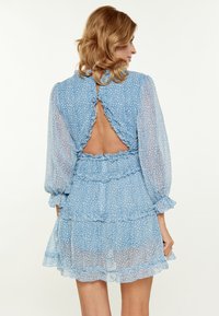 Rochie de culoare bleu deschis, cu un model floral, maneci transparentă, detalii cu volane și spate descoperit. Design cu straturi, în trepte, până la genunchi.