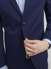 Mörkblå blazer med en ensam svart knapp, nyckelkragar och en ficka. Den har en slät textur med en skräddarsydd passform.