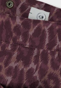 Tissu maroon à motifs avec une apparence texturée, présentant un bouton et une boucle en tissu, mettant en valeur un mélange de tons clairs et foncés.
