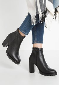 Bottines noires en cuir avec une finition texturée, talon bloc haut et fermeture éclair sur le côté ; semelle extérieure robuste avec un profil prononcé pour une meilleure adhérence.