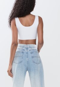 Hvid kort tanktop med en rund udskæring i ryggen parret med lyseblå højtaljede denimjeans med en bleget vask og baglommer.