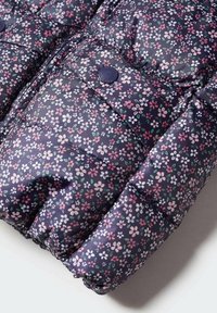 Doudoune florale avec une base bleu marine ornée de motifs de fleurs roses et blanches. Confectionnée en tissu lisse avec des sections matelassées et des boutons pression.