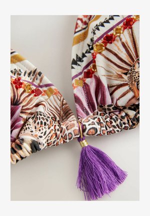 Țesătură colorată cu imprimeu animal și modele geometrice, finisată cu o accent de ciucure mov și detalii din hardware auriu.
