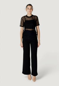 Top de malla negra transparente con mangas cortas, superpuesto sobre tejido opaco; combinado con pantalones de pierna ancha en negro; tacones en tonos neutros.
