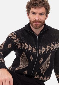 Schwarz-beigefarbener, gemusterter Cardigan mit Reißverschluss und geometrischen Mustern, einem hohen Kragen und gerippten Bündchen, gefertigt aus strukturiertem Strickstoff.