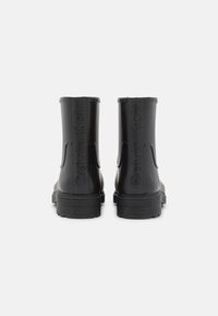 Botas de tobillo de goma negra con un acabado mate, que presentan una marca grabada, paneles laterales elásticos y una suela gruesa con relieve.