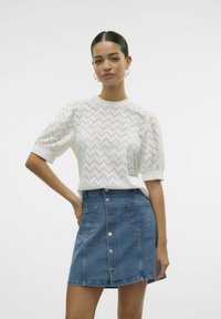 Hvid bomuldsbluse med zigzag mønster, puffede ærmer, parret med en blå denim A-line nederdel med frontknapper og lommer.