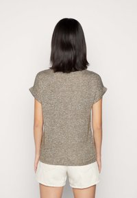 Hnědý krátký rukáv pletený top s texturovaným povrchem. V kombinaci se světlými šortkami s manžetou. Pohled zezadu.