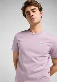 Lila t-shirt med kort ärm i mjukt material. Har en liten rektangulär logotypapa på vänster bröst. Avslappnad passform, slät yta.
