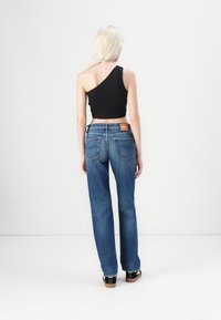 Top corto negro de un solo hombro, combinado con jeans ajustados de mezclilla azul con bolsillos traseros y una etiqueta de marca en la pretina.